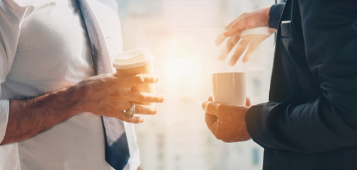 business background of hands holding coffee cups of two businessman standing together during having business talking