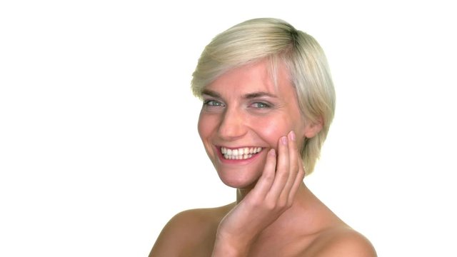 Close up shot of a blonde, short-haired woman, smile and resting her hand upon her face in a studio with a seamless white background