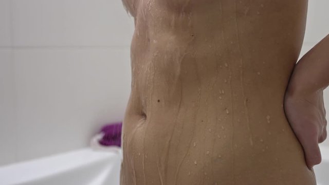 Woman with six pack drips water over her stomach in shower,slow motion