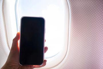 Mocku image of female hands holding smartphone with a blank desktop screen next to an airplane window. Black screen mobile phone