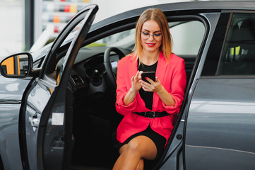 Beautiful young woman buys a car in the dealership saloon.