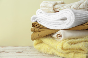 Set of warm winter clothes on table against color background