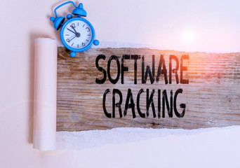 Text sign showing Software Cracking. Business photo showcasing modification of software to remove or disable features Alarm clock and torn cardboard placed above a wooden classic table backdrop