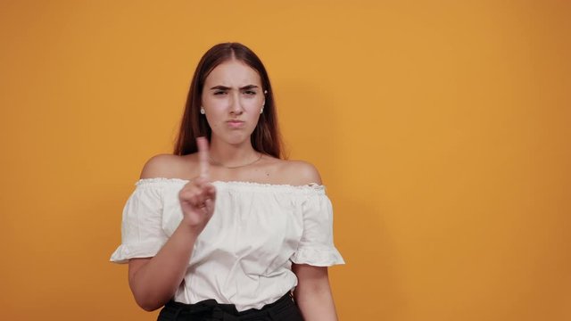 Serious young woman doing stop, pouse gesture isolated on orange background in studio in casual white shirt. People sincere emotions, lifestyle concept.