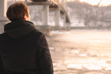 Back view of thoughtful young man standing by river in winter