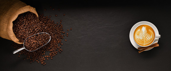 Cup of coffee latte and coffee beans in burlap sack on black background