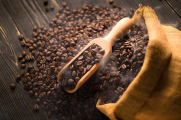 Top view of coffee beans in wooden spoon with smoke on pile of coffee beans