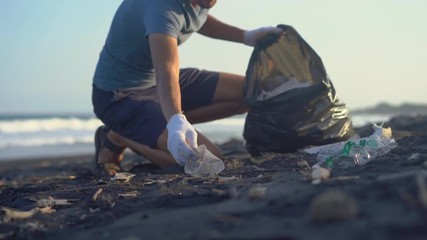 Young man clean up the beach from a trash - Powered by Adobe