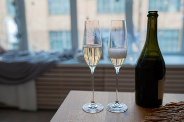 two mother-of-pearl glasses with champagne, bubbles and foam next to a dark glass bottle against a...