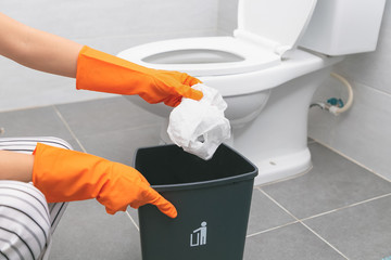 Hands holding the tissue paper for tipping into the trash in the toilet.