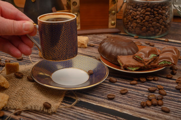 The girl's hand holds a Cup of coffee over a wooden table with brown sugar, coffee beans and chocolate.