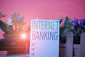 Writing note showing Internet Banking. Business concept for banking method which transactions conducted electronically Flowers and writing equipments plus plain sheet above textured backdrop