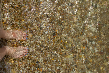 Barefeet with Blue Toenails Standing on Pebbles in Shallow Water