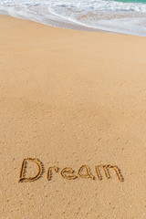 The word Dream written in the sand on the beach with a wave washing in