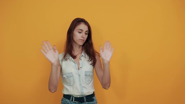 Young woman in blue denim shirt keeping hands crossed, looking directly on orange background in studio. People sincere emotions, lifestyle concept.