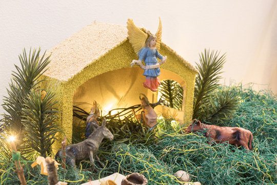 Christmas Manger and yellow lights whit yellow house and angel on top, green grass, grey donkey and brown ox, Holy Mary and Joseph toys.