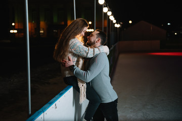 Young couple in love, date at the ice rink, a girl sitting on a guardrail and kiss with her...