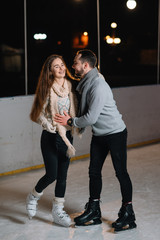 Winter skates, loving couple holding hands and rolling on rink. Illumination in background, night. Concept training.