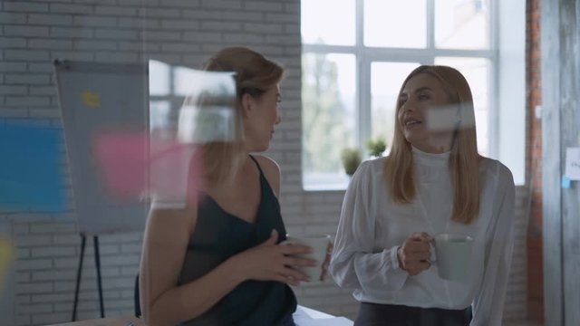 Two successful happy business partners communicate and laugh during a lunch break in the office. women drink coffee and have fun talking 4K