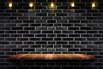 Empty brown plank wood shelf at black brick wall background with light bulbs string,Mockup for display or montage of product or design.