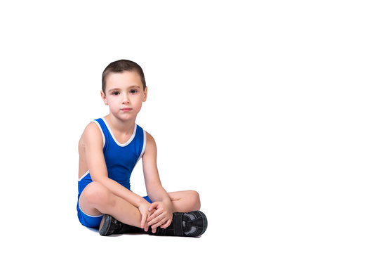 Sporty cheerful boy in a blue wrestling tights is ready to engage in sports exercises, is sitting on the floor on a white isolated background