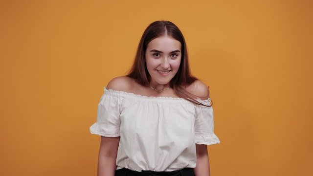 Cheerful caucasian young woman keeping fists up, waiting for special moment isolated on orange background in studio in casual white shirt. People sincere emotions, lifestyle concept.