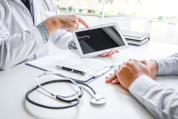 Doctor consulting with patient presenting results on digital tablet tablet sitting at table