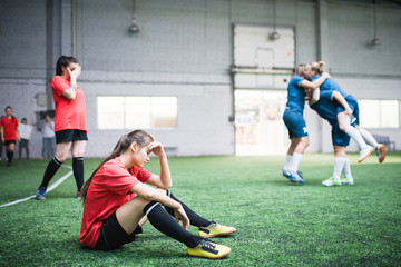 Fototapeta premium Tired young female football player and other girls resting after game