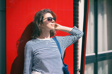Portrait of a young woman in sunglasses on a background of red window shutters.