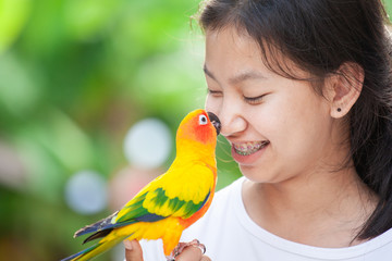 Beautiful little parrot birds standing on woman hand. Asian teenager girl play with her pet parrot...