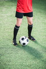 Soccer ball between legs of active girl in sports uniform standing on field