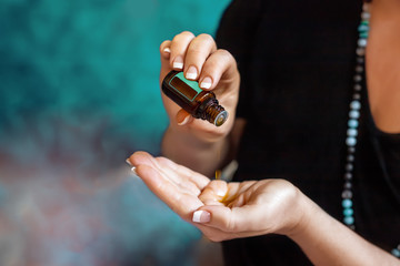 Womans hand with essential oil dropping to her palm, mint blue beads and background