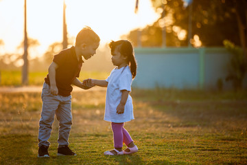 Asian siblings big brother and young sister holding hand and playing in the park together at sunset...