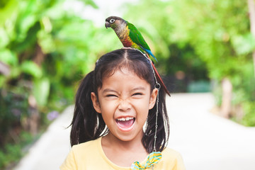 Beautiful little parrot birds standing on child head. Asian child girl play with her pet parrot...