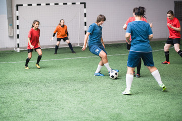 Obraz premium Young active female players in blue and red sportswear attacking soccer ball