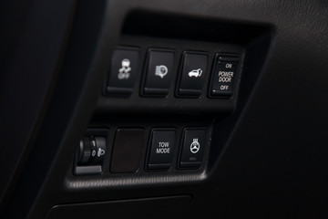 Close-up on a part of the interior of a modern luxury car with a view of the heated steering wheel, trunk open, stability system buttons with black trim elements