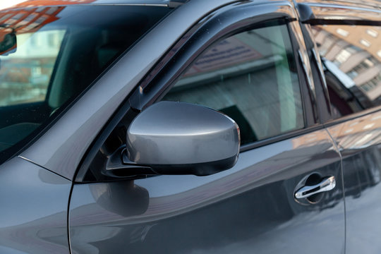 Close-up of the side left mirror without turn signal repeater and window of the car body gray SUV on the street parking after washing and detailing in auto service industry. Road safety while driving