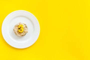 Cat's birthday concept. Pet feed with festive candle in shape of three on yellow background top-down copy space