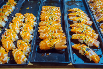 Rows of japanese sushi food. Maki ands rolls with tuna, salmon, shrimp, crab and avocado. Top view of assorted sushi in black plastic container being sale at market. Selective focus.