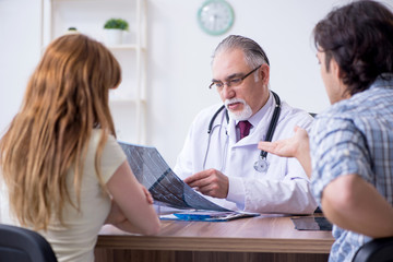 Fototapeta premium Young couple visiting old male doctor