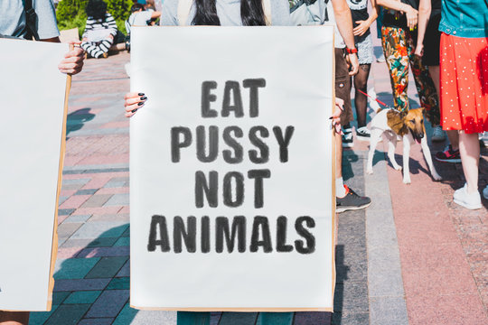 The phrase "Eat pussy not animals" on the big white cardboard in the women's hands. Crowd. Animal rights. March. Rally