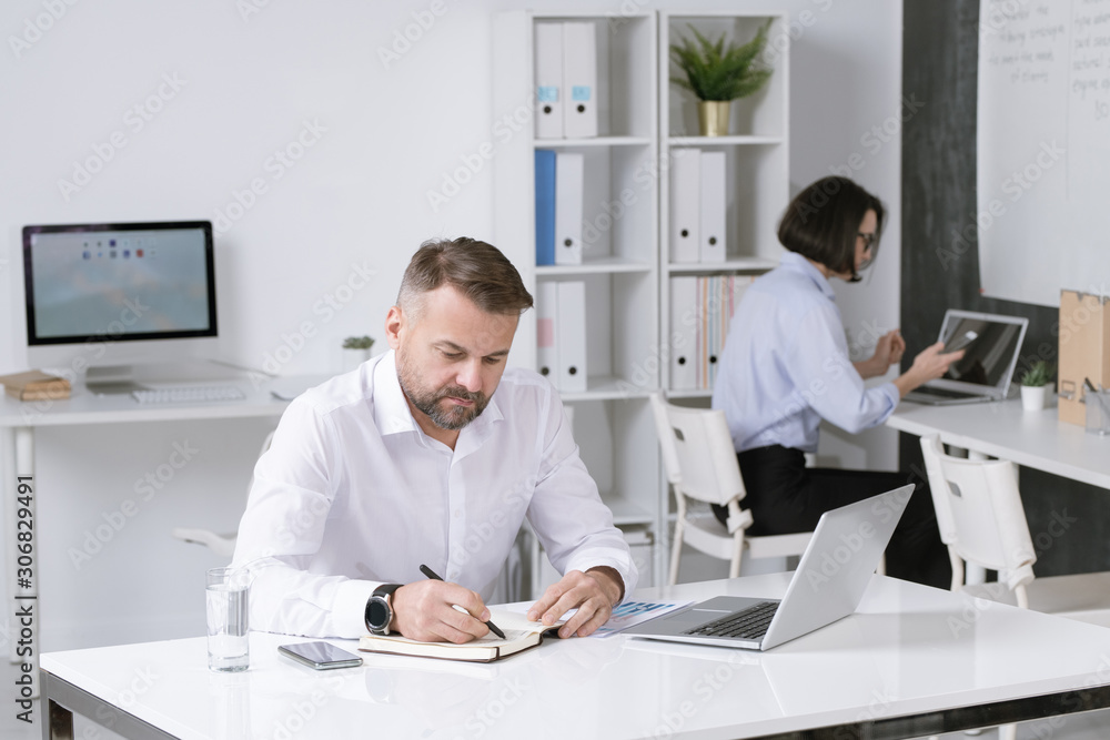 Poster serious bearded employer thinking of new ideas and making notes in notebook