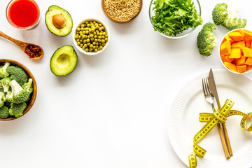 Diet concept. Fork and knife tied with measure tape on plate near vegetables on white background top view copy space