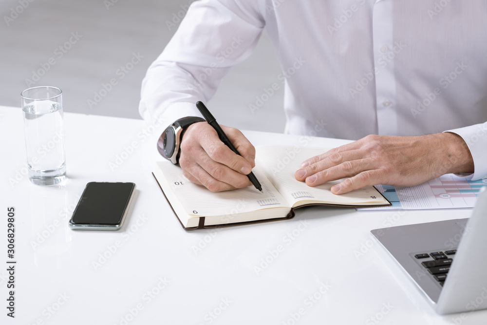 Poster hands of employer with pen over page of notebook writing down plan for the day