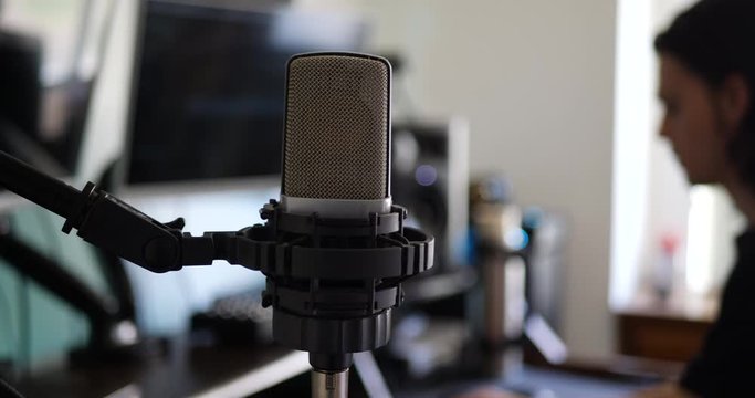 A male music producer at his music recording studio desk with a condenser microphone for recording a singer or vocalist SLIDE LEFT.