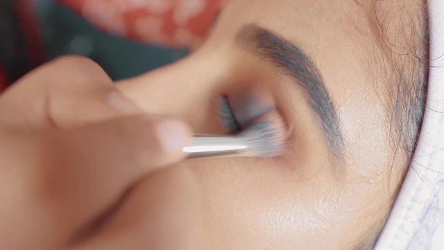 Close up of woman's eye and make up artist putting eye shadow with make up brush on her eye 