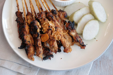 Goat satay with rice cake and peanut sauce, traditional food from Yogyakarta, Indonesia on the wooden table.