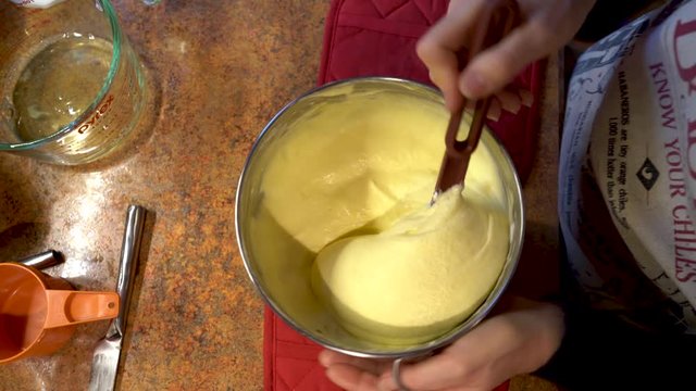 Mature woman stirring sabayon mixture for tiramisu in a home kitchen.