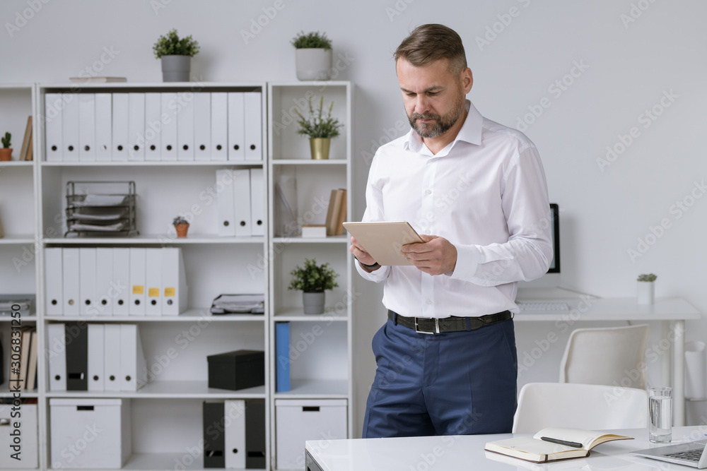 Poster confident mature entrepreneur scrolling in tablet while searching for data