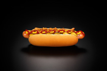 Danish hot dog with pickled cucumbers, fried onions, ketchup and mustard on a black background.